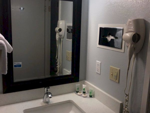 A bathroom sink with a white countertop, black-framed mirror, wall-mounted hair dryer, and a frosted glass light fixture above.