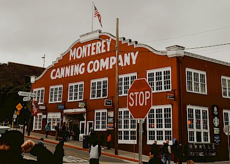 A red brick building with a white sign reading &ldquo;Monterey Canning Company,&rdquo; a stop sign in front, and power lines overhead, daytime.