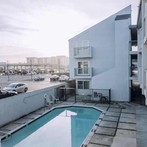 A small rectangular outdoor pool on a tiled deck with a pale blue building and city street in the background, at a sunny time of day.