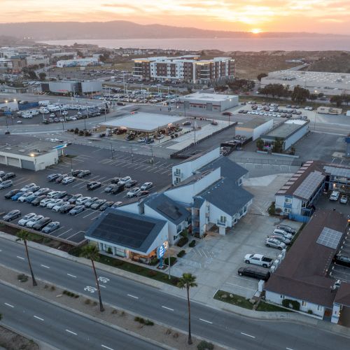Aerial view of a small town area with a church, parking lots, and several low-rise buildings along a main road at sunset, calm and expansive.