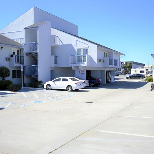 A row of modern cars lined up outside white, angular buildings on a sunny day, with blue skies and a wide concrete lot.