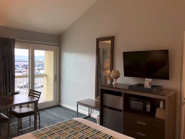 Cozy hotel room with a balcony, a desk and dresser, wall-mounted TV, and a windowed door to an outdoor balcony, overlooking a distant view.